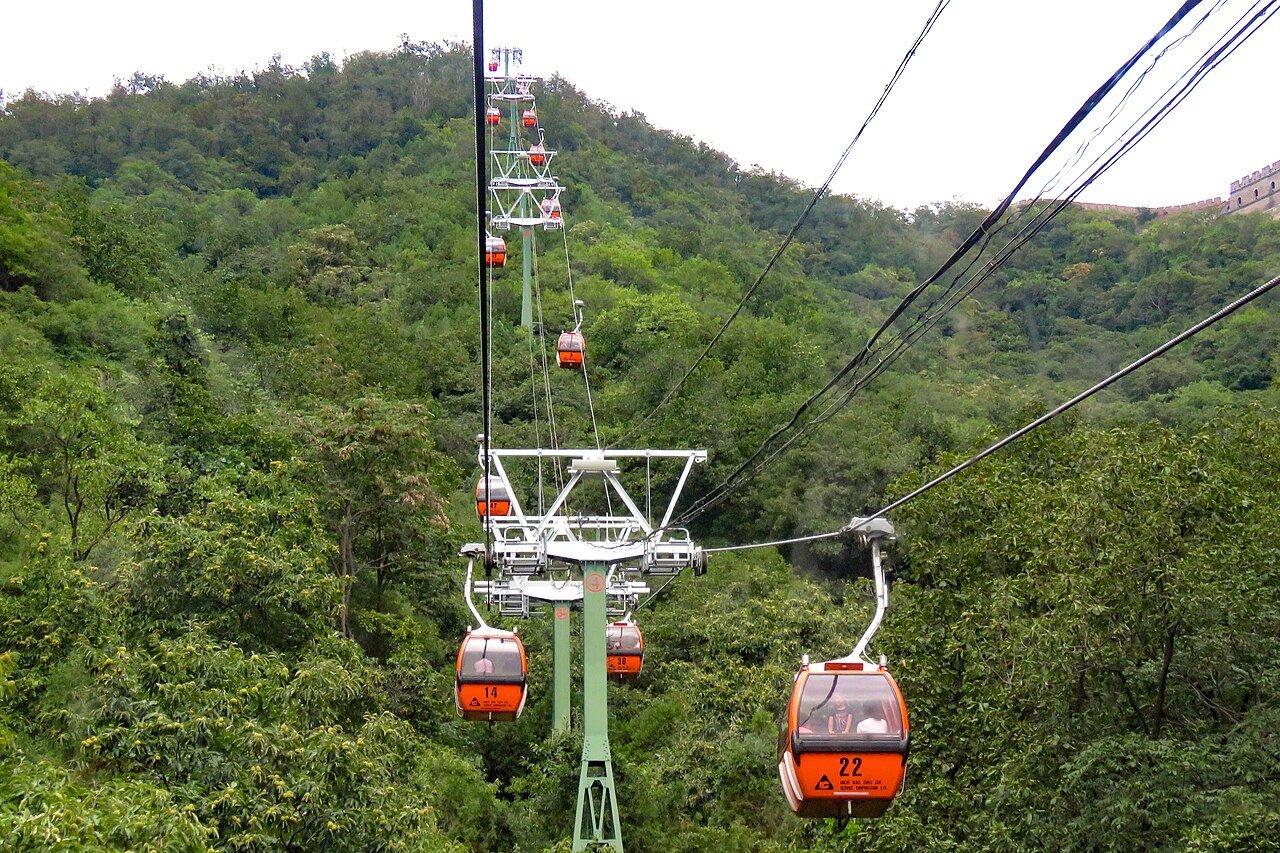 Orange gondolas of the Mutianyu cable car climbing the wooded slope toward the Great Wall