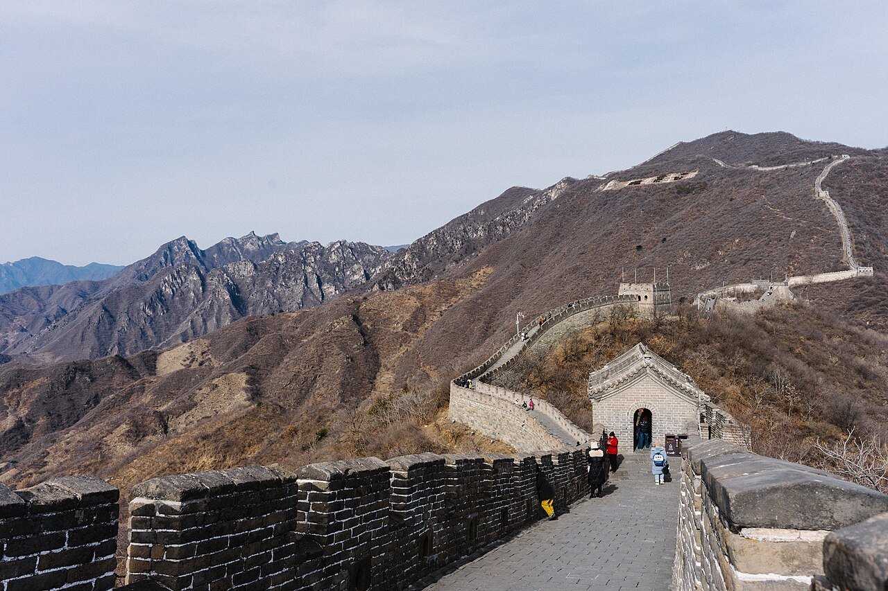 Walking the paved wall at Mutianyu with a gate tower ahead and mountains beyond